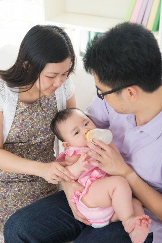 Asian father feeding baby with bottle with asian mother watching