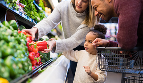 mixed race family in fresh vegetable section of food store