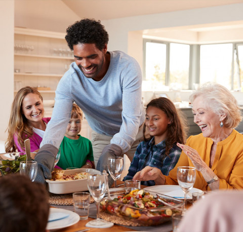 image of a man putting down a casserole dish on a dinner table that is full of waiting people