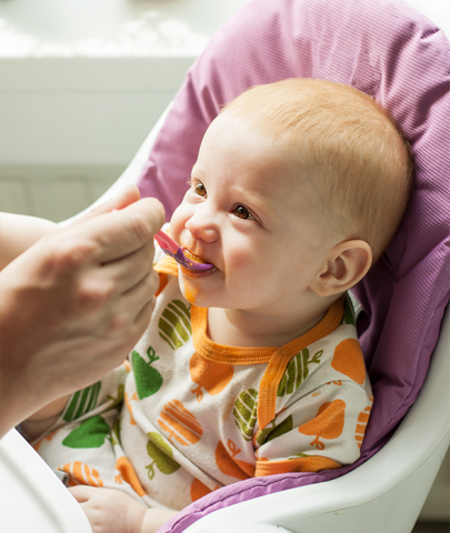 happy baby eating orange food in high chair