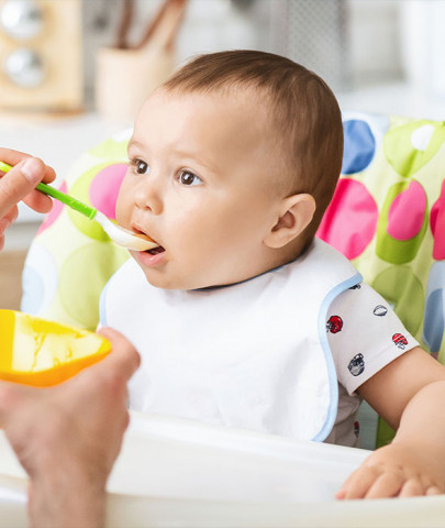 adult male feeding white baby in highchair with spoon