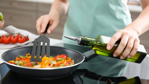 Woman pouring oil into frying pan on stove
