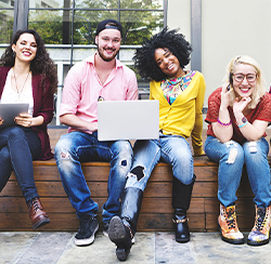 picture of young adults sitting on a ledge with a laptop and smiling