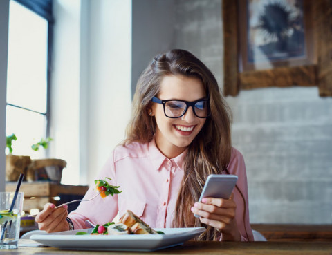 young girl eating salad while looking at her cell phone