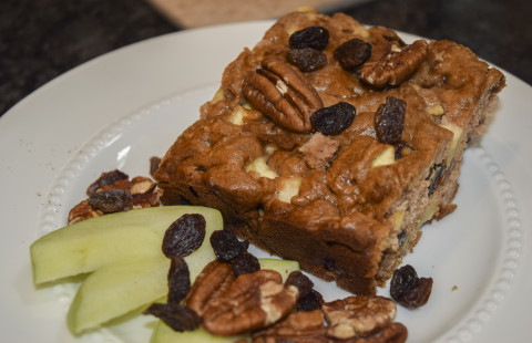 slice of apple coffee ccake on a plate with apples, pecans, and raisins