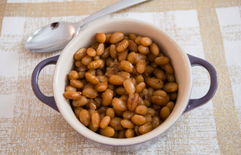 small crock of baked beans on a cloth placemat with a spoon