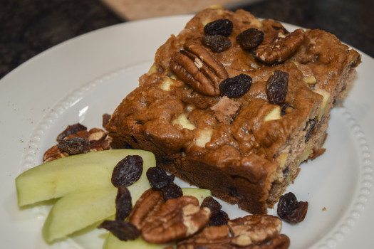 slice of apple coffee ccake on a plate with apples, pecans, and raisins