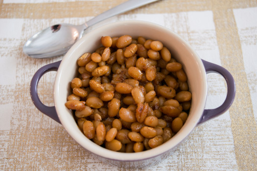 small crock of baked beans on a cloth placemat with a spoon