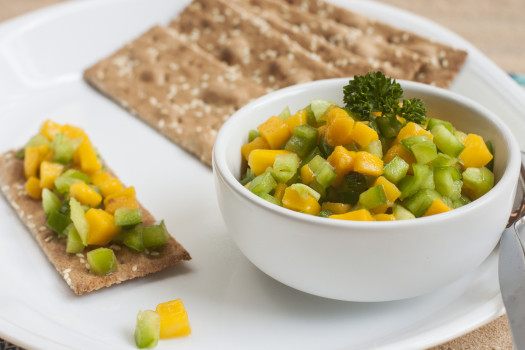 Small bowl of easy mango salsa on a plate of whole grain crackers