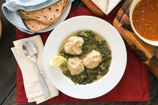 bowl of dumplings in a broth with cooked greens with a plate of flat bread in the background