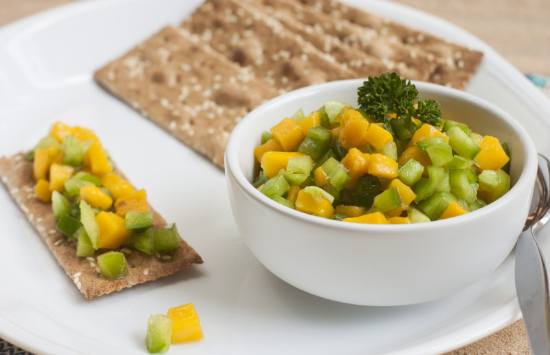 Small bowl of mango salsa on a plate of whole grain crackers